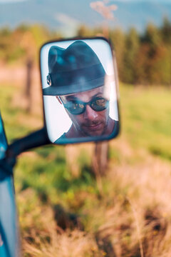Reflection in rear-view mirror of man wearing a hat and sunglasses