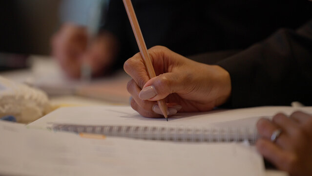 Close up a person's hand holding a pencil writing in a notebook in meeting room at office