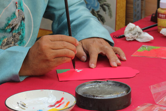 Calligraphy master hand painting red envelope with brush, artist writing lucky money pocket for lunar new year tet festival tradition, Vietnam
