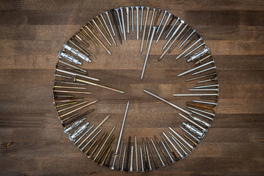 Circle made of various screws and nails on brown wood texture. Industrial flat lay. Carpentry still life.