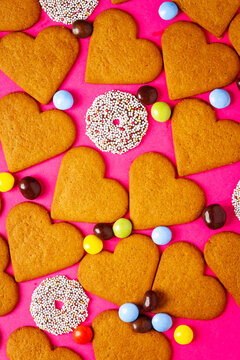 Top view of candies and heart shaped cookies on a vibrant pink background. Dessert photography, sweet treats.