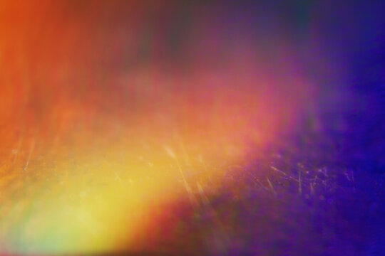 Extreme close up of abstract vibrant iridescent holographic rainbow foil background with lens flare. Glitter surface. Selective soft focus, shallow depth of field.