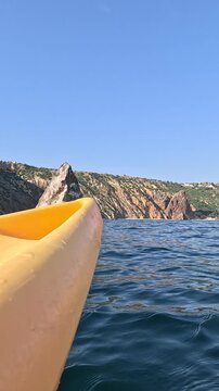 Mediterranean seascape navigation highlights yellow vessel bow. Low angle POV captures smooth drift along rocky crags under bright sun.