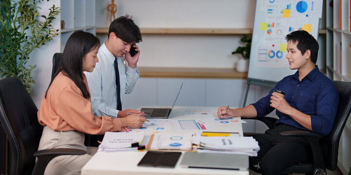 Diverse Asian business team collaborating at office desk during strategic planning meeting