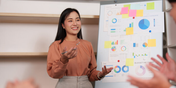 Smiling Asian businesswoman presenting strategic project on whiteboard in office meeting