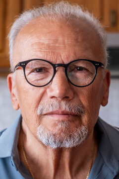 Senior man with white hair and beard wearing black round glasses, looking directly at the viewer with a thoughtful expression, representing aging and wisdom
