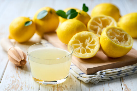 homemade lemon juice in a glass on table. Freshly squeezed lemon juice in a glass with halved lemons on white table, selective focus.