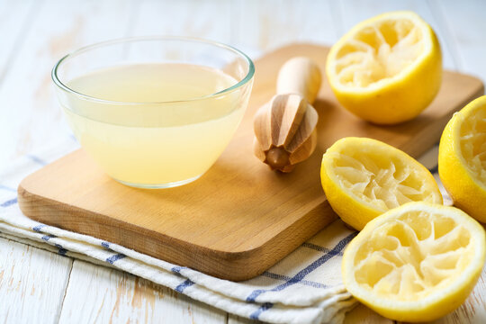 Freshly squeezed lemon juice in a bowl with halved lemons on white table, selective focus. Organic lemon juice in a bowl on table.