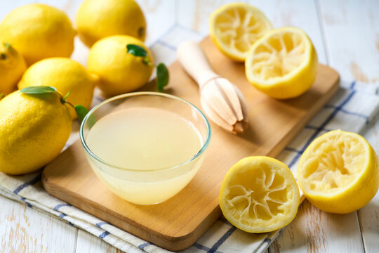 Bowl with fresh lemon juice, squeezer and ripe lemons on white table, close up. Homemade lemon juice in a bowl on table.