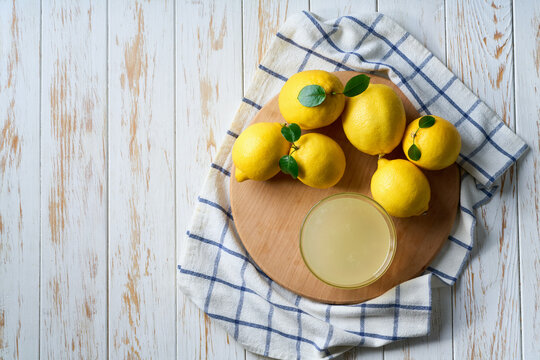 homemade lemon juice in glass and ripe lemons on white wooden table, with copy space for text. Top vie