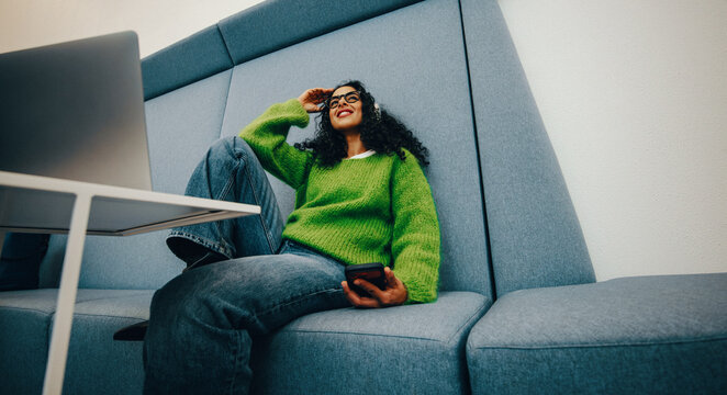Woman relaxing in casual workspace with smartphone and laptop