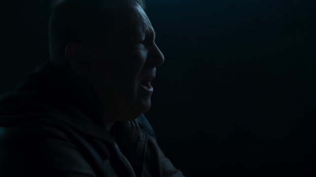 Older man speaking in side profile against dark background as facial expression changes
