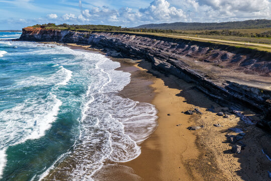 Aerial view of the rugged rocky cliffs and sandy shoreline of Lake Arragan Beach, featuring the Pacific Ocean, exposed coastal rock formations and natural bushland within Yuraygir National Park