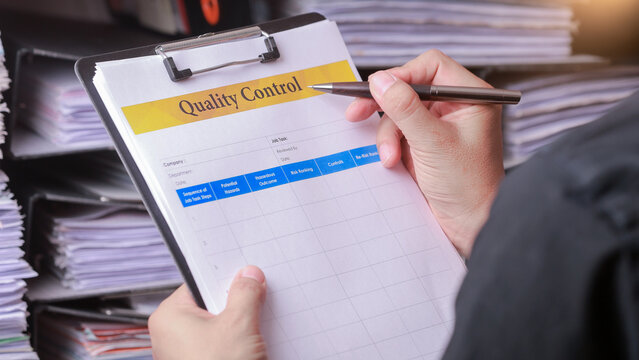 Focused auditor holding clipboard with document to check report during quality control inspection in busy office space