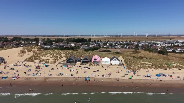 Drone tracking shot panning from right to left across the paradisiacal Camber Sands beach, England. Cinematic landscape composition on a clear blue sky day with wind turbines on the horizon