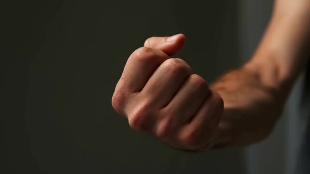 Clenched fist held near dark wall in closeup indoor scene with arm visible