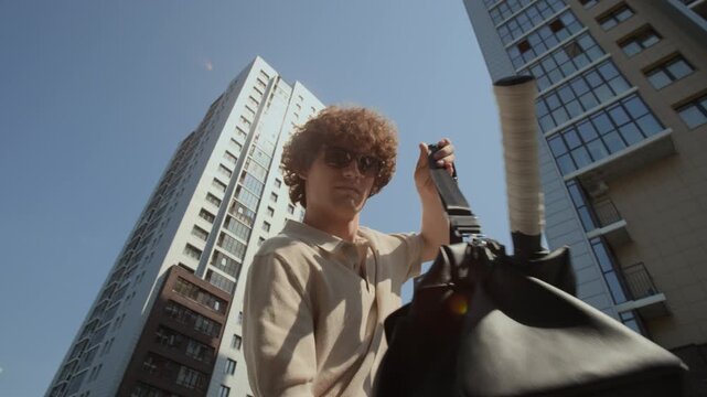 POV of young adult Caucasian man wearing sunglasses putting tennis bag into car trunk and closing lid, low angle view. Footage is suitable for active lifestyle and sports equipment promotions