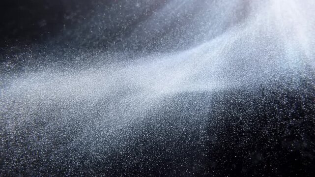 Fine underwater bubbles and particles suspended in dark water beneath bright light