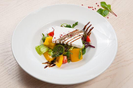 Greek salad with thick slice of feta cheese, fresh vegetables, olives, and balsamic glaze on white plate