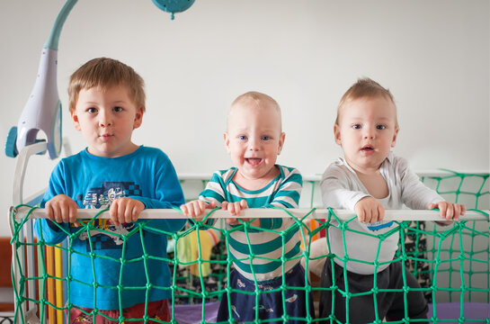 Three brothers share a joyful, wonder-filled moment together at their crib in a bright, sunlit room