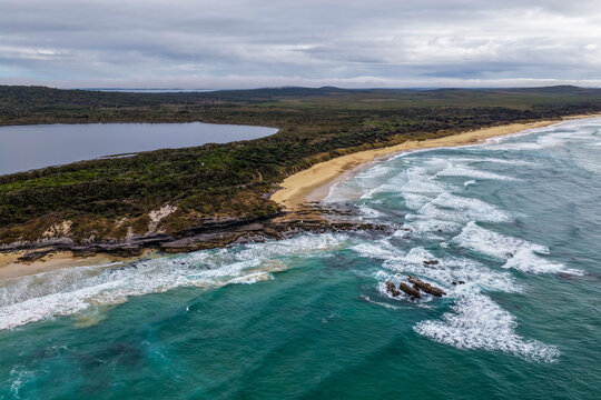 Aerial view of Lake Arragan Beach and the surrounding coastal landscape, featuring a long sandy shoreline, Pacific Ocean, native bushland and pristine natural scenery within Yuraygir National Park 