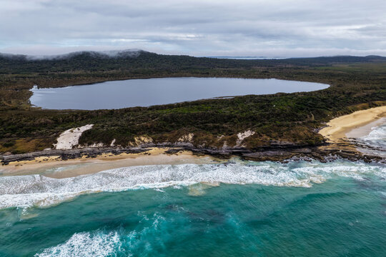 Aerial view of Lake Arragan Beach and Lake Arragan within Yuraygir National Park, showcasing the sandy Pacific coastline, coastal lake, native bushland and surrounding natural landscape 