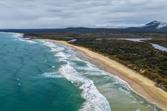 Aerial view of Lake Arragan Beach and the surrounding coastal landscape, featuring a long sandy shoreline, Pacific Ocean, native bushland and pristine natural scenery within Yuraygir National Park