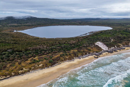 Aerial view of Lake Arragan Beach and Lake Arragan within Yuraygir National Park, showcasing the sandy Pacific coastline, coastal lake, native bushland and surrounding natural landscape 