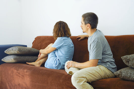 Woman sitting on couch hugging her knees while man turns toward her to reconnect. Captures first step toward reconciliation, empathetic partner approach, and nonverbal relationship repair attempt.
