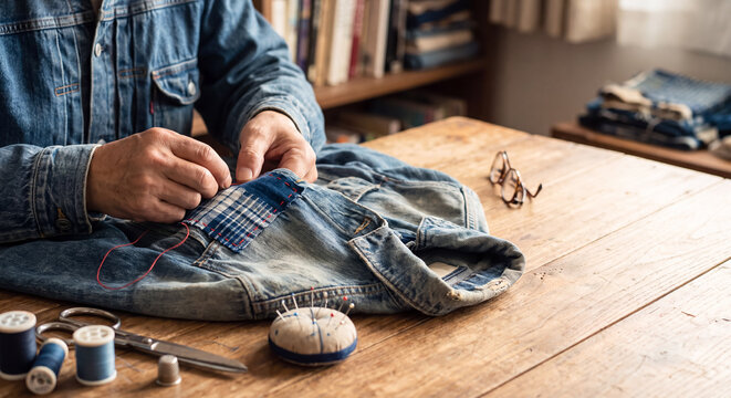 Person repairing a denim shirt using thread and needle in a cozy workspace