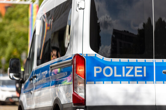 German police van stands near CSD event in Magdeburg with rainbow colors reflected in side windows and bodywork. Visible Polizei marking represents security, crowd safety and urban policing