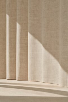 Closeup of an undyed linen curtain shows its fine woven texture, natural slubs and vertical folds as sunlight passes through the fabric and creates a softly illuminated neutral surface