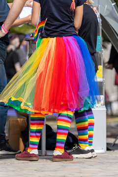 Person wearing rainbow tulle skirt, striped socks and pride flag stands at outdoor CSD event in Magdeburg. Bright multicolor clothing expresses LGBTQ identity, diversity, visibility and inclusion