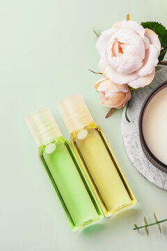 Cosmetic beauty bottles with pink rose decoration and aroma candle on green background, top view