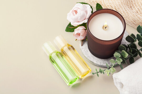 Body massage oil bottles with burning aroma candle, pink rose and green leaves decoration, spa and wellness background