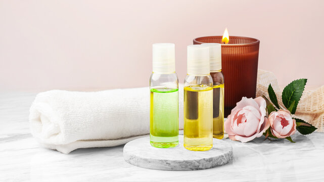Body oil bottles with aroma candle, towel and pink roses on marble table, spa and wellness background