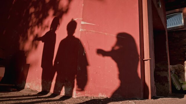 Shadows of diverse young adults posing and filming social media content with smartphone projected on red wall outdoors. Footage is ideal for youth culture and digital marketing campaigns