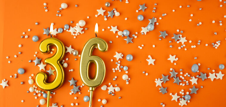 Birthday or anniversary celebration concept. Candles in the shape of the number thirty-six on an orange background among decorative ornaments. 36th anniversary. Banner