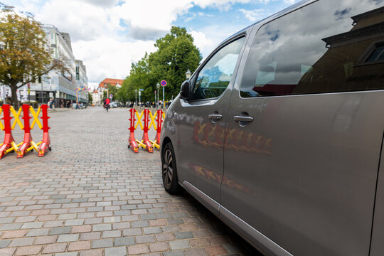 Gray van passes beside portable red and yellow security barriers placed across cobblestone street. Temporary traffic control and vehicle restriction protect pedestrian zone during event in Magdeburg