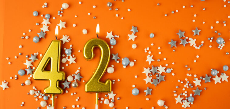 Birthday or anniversary celebration concept. Candles in the shape of the number forty-two on an orange background among decorative ornaments. 42nd anniversary. Banner