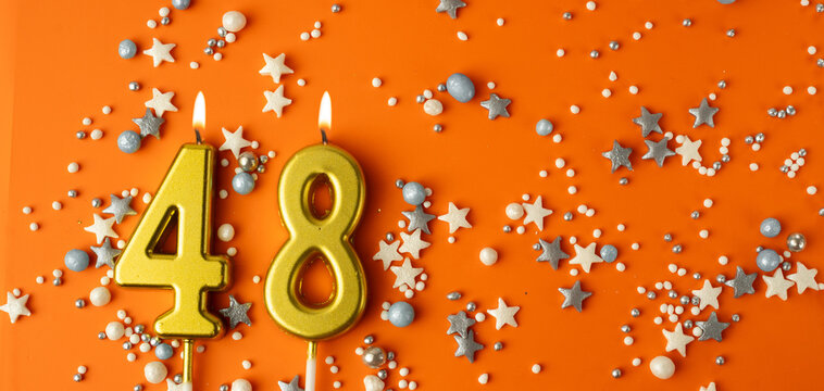 Birthday or anniversary celebration concept. Candles in the shape of the number forty-eight on an orange background among decorative ornaments. 48th anniversary. Banner