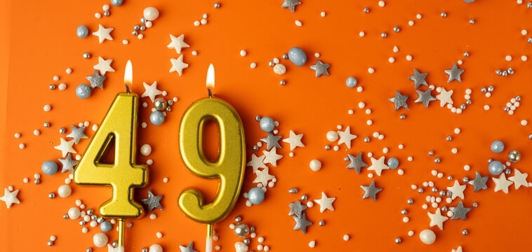 Birthday or anniversary celebration concept. Candles in the shape of the number forty-nine on an orange background among decorative ornaments. 49th anniversary. Banner