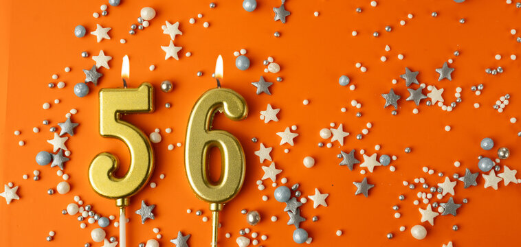 Birthday or anniversary celebration concept. Candles in the shape of the number fifty-six on an orange background among decorative ornaments. 56th anniversary. Banner
