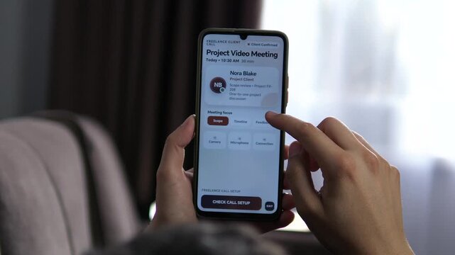 Freelancer prepares a smartphone video meeting with a client, checking camera and microphone before a project discussion on scope, timeline and feedback.