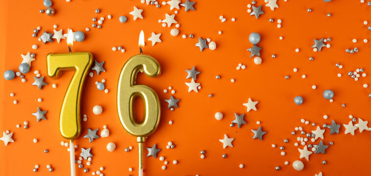 Birthday or anniversary celebration concept. Candles in the shape of the number seventy-six on an orange background among decorative ornaments. 76th anniversary. Banner