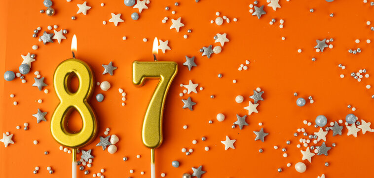 Birthday or anniversary celebration concept. Candles in the shape of the number eighty-seven on an orange background among decorative ornaments. 87th anniversary. Banner