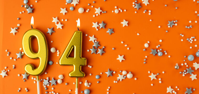 Birthday or anniversary celebration concept. Candles in the shape of the number ninety-four on an orange background among decorative ornaments. 94th anniversary. Banner