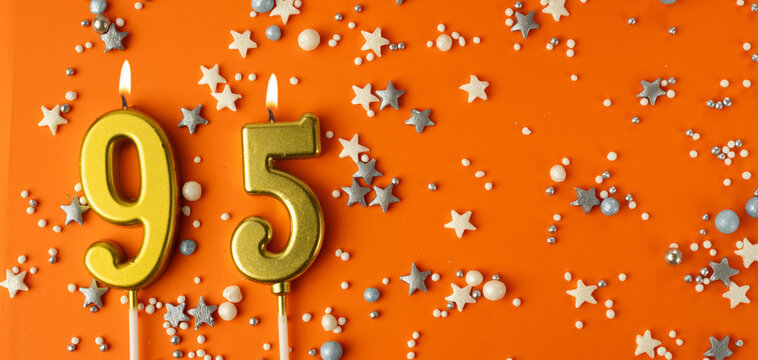Birthday or anniversary celebration concept. Candles in the shape of the number ninety-five on an orange background among decorative ornaments. 95th anniversary. Banner