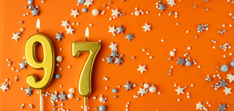Birthday or anniversary celebration concept. Candles in the shape of the number ninety-seven on an orange background among decorative ornaments. 97th anniversary. Banner
