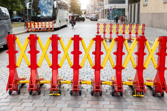 Expandable red and yellow security barriers block cobblestone street while coach waits behind temporary checkpoint. Urban traffic control creates protected route during public event in Magdeburg